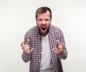 Portrait of aggressive bearded young man in plaid shirt standing with furious face full of hatred and anger, experiencing strong emotions, shouting